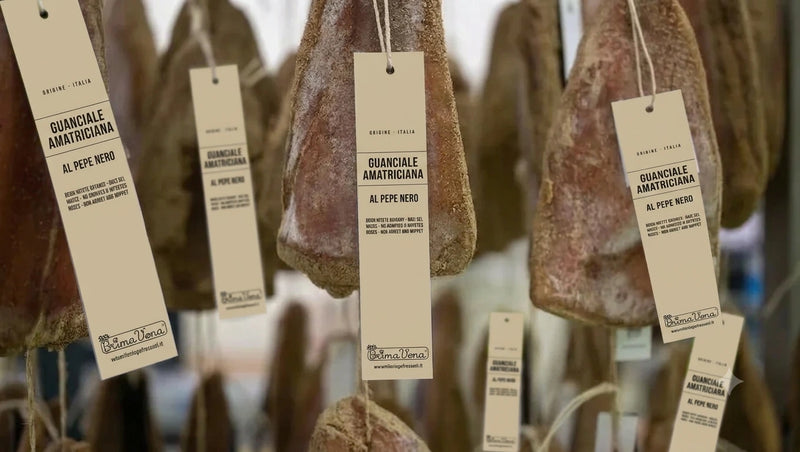 Pedrazzoli organic guanciale curing on hooks, each piece tagged Amatriciana al Pepe Nero